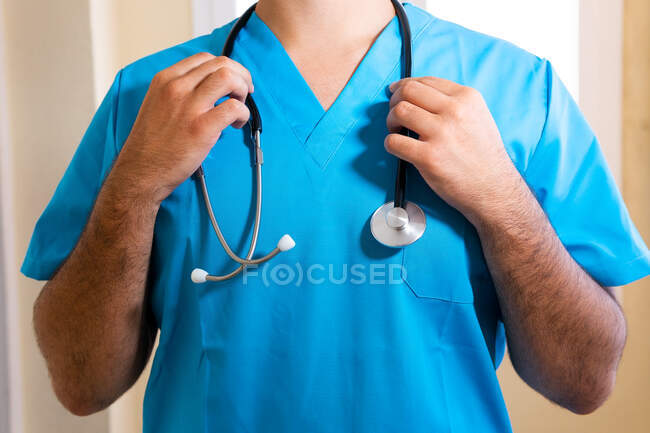Анонімний чоловічий лікар у блакитній формі та зі стетоскопом, що стоїть у клініці — стокове фото