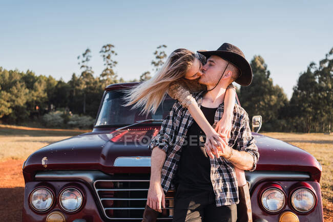Молодая пара влюбленных сидит в красном винтажном пикапе и целуется на закате летом — стоковое фото