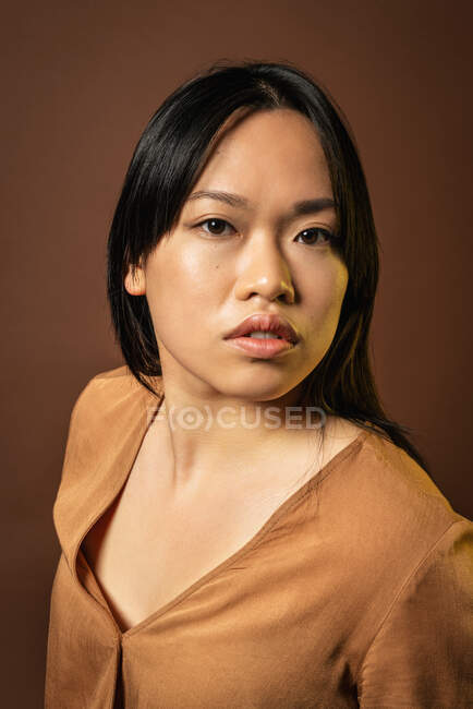 Vue de face de la femelle asiatique en vêtements à la mode regardant la caméra sur fond brun en studio — Photo de stock