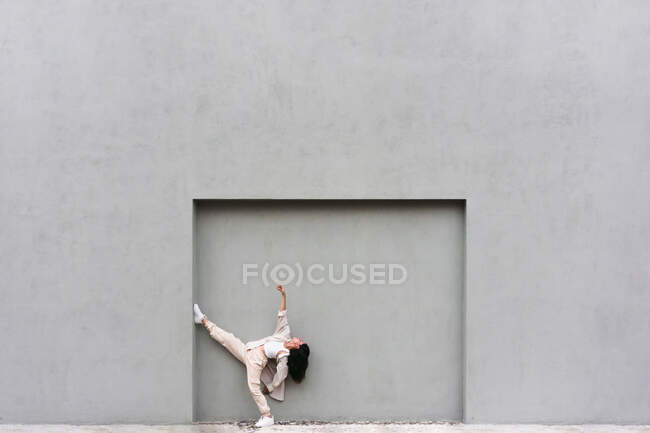 Kreative coole Frau lehnt an grauer Wand und tanzt ausdrucksstark in der City Street — Stockfoto