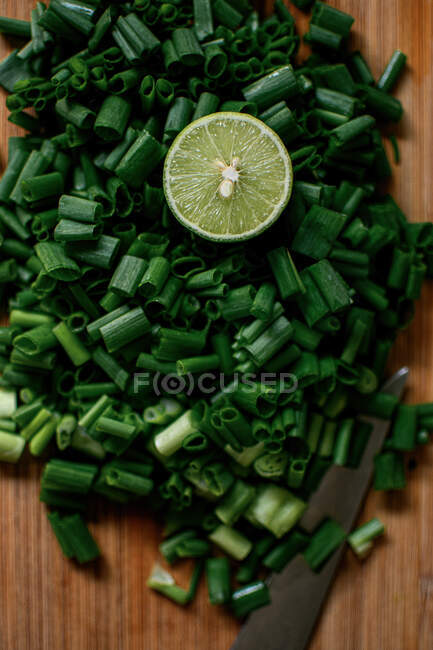 Vue de dessus de l'oignon vert haché et la moitié de la chaux fraîche placée sur la planche à découper en bois dans la cuisine — Photo de stock
