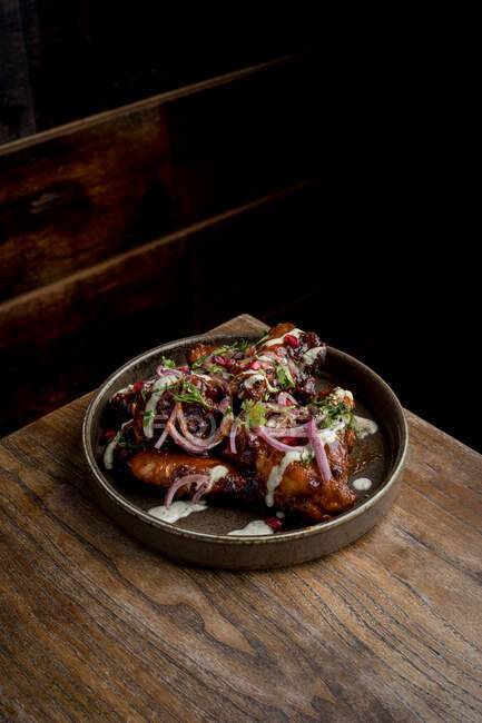 Зверху смачні смажені курячі крильця в соусі барбекю, прикрашені свіжими овочами, які подаються на тарілці на дерев'яному столі в ресторані — стокове фото