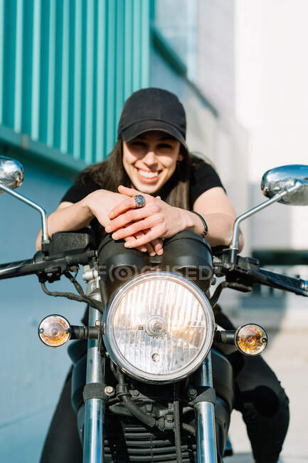 Positivo motociclista femminile seduto sulla moto parcheggiata in strada nella giornata di sole e guardando la fotocamera — Foto stock