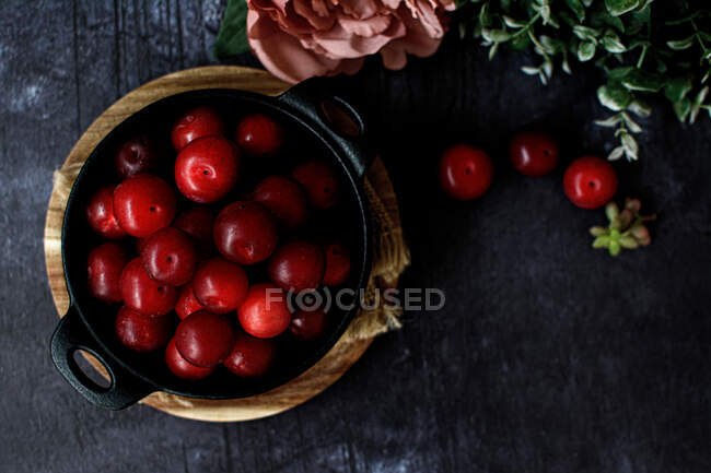 Vue du dessus du bol avec des prunes fraîches sucrées servies sur une table noire — Photo de stock