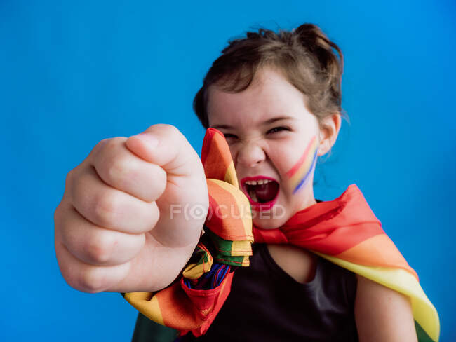 Гарненька щаслива дитина з різнокольоровими пов'язками на шиї і зап'ясті стоячи навпроти синього фону і дивлячись на камеру — стокове фото