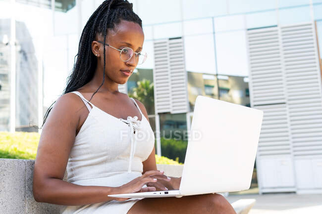 Позитивна афро-американська жінка сидить з ноутбуком на вулиці в Барселоні, дивлячись на екран — стокове фото