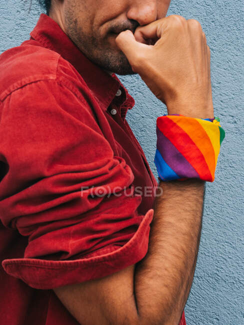 Cultivé mâle homosexuel ethnique serein méconnaissable avec bandana arc-en-ciel sur la main montrant biceps sur fond de mur gris en ville — Photo de stock