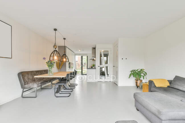 Interior design del moderno appartamento open space con comodi divani nella zona salotto vicino a grandi finestre e zona pranzo con tavolo e sedie sotto la lampada — Foto stock
