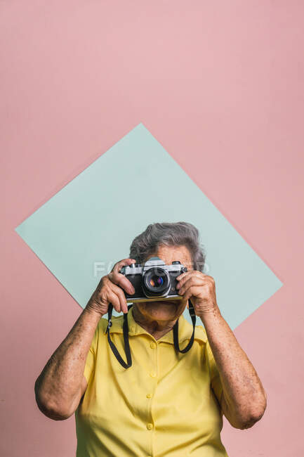 Moderna femmina anziana scattare foto su fotocamera vintage su due sfondo colorato in studio — Foto stock