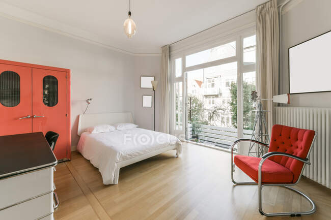 Modern home interior design of spacious bedroom with large window furnished with bed and wardrobe and armchair with loft style lamp — Stock Photo