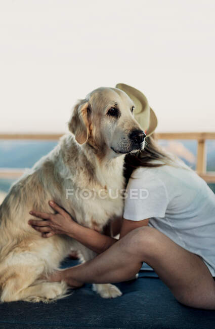 Босоногая женщина обнимает верную собаку Золотистого ретривера, сидя на кровати в фургоне во время путешествия на природе — стоковое фото