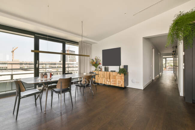 Table à manger et chaises placées près d'une grande fenêtre panoramique dans une chambre spacieuse avec TV et armoire dans un appartement moderne de style loft — Photo de stock