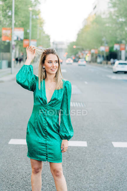 Mulher despreocupada em vestido verde na moda de pé com um braço levantado na rua e olhando para longe — Fotografia de Stock