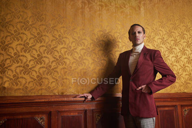 Confident adult male actor in elegant classy clothes keeping hand in pocket and looking away thoughtfully while standing near wall in vintage style room — Stock Photo