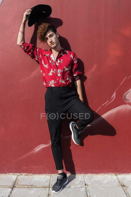 Junger eitler Mann in schicker Kleidung steht mit erhobenem Bein auf gefliestem Gehweg und blickt auf der Straße in die Kamera — Stockfoto