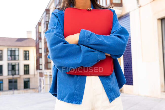 Cortado irreconocible freelancer femenina con netbook en caja roja de pie en la calle de la ciudad y mirando hacia adelante - foto de stock