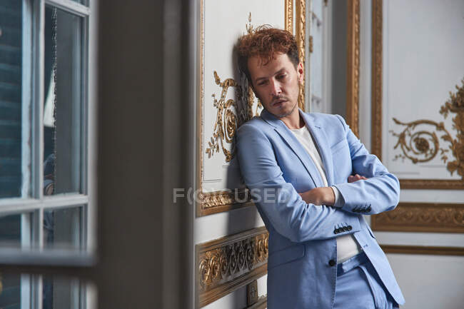 Stressed male in suit standing with crossed arms and leaning on wall in posh room — Stock Photo