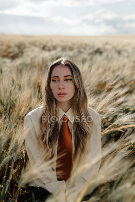 Young female with wavy hair looking away in countryside field under cloudy sky on blurred background — Stock Photo