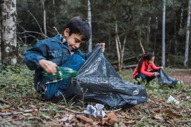 Етнічні волонтери з пластиковими пакетами збирають сміття з місцевості проти дерев в літньому лісі в денний час — стокове фото