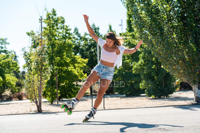 Young fit female in rollerblades showing stunt on road in city in summer — Stock Photo