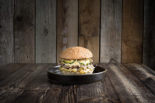 Délicieux hamburger avec viande chaude et fromage savoureux servi sur une assiette noire sur une table en bois — Photo de stock