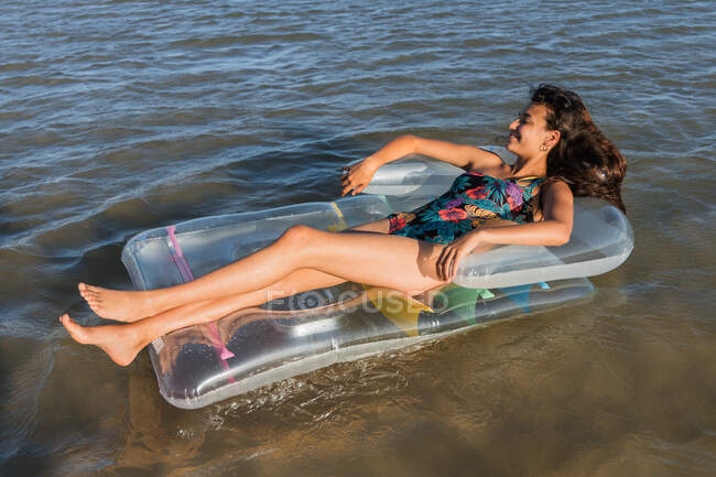 Contenido hembra acostada en colchón inflable flotando en el agua de mar en el día soleado en verano y mirando hacia otro lado - foto de stock
