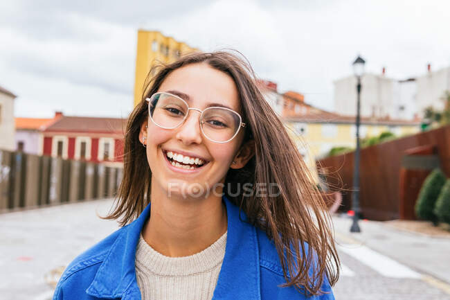 Smiling female with flying hair walking along road in city on windy day — Stock Photo
