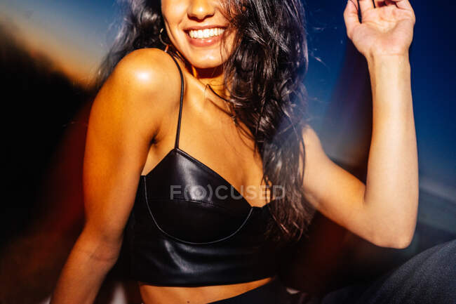 Привлекательная молодая длинноволосая латиноамериканская брюнетка в черном топе сидит в машине с легким отражением в ночное время — стоковое фото