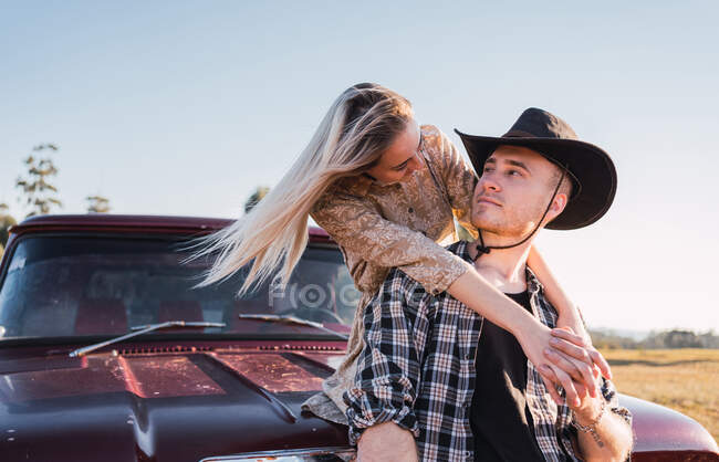 Vista lateral do casal na moda no amor abraçando perto estacionado carro pickup retro vermelho no dia ensolarado no verão — Fotografia de Stock