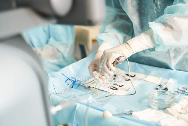 Cosecha enfermera irreconocible en uniforme estéril preparando instrumentos médicos para la cirugía en la mesa en el hospital - foto de stock