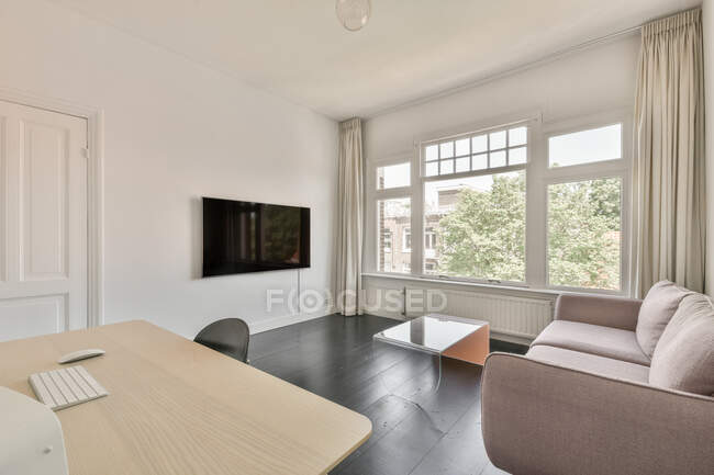 Bequemes Sofa vor dem Fernseher an weißer Wand in der Nähe eines großen Fensters in der Wohnung mit modernem minimalistischem Interieur — Stockfoto