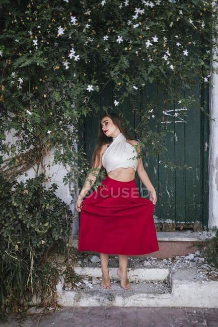 Mujer elegante con labios rojos y en traje de verano cerca de flores aromáticas que crecen en el patio de la casa - foto de stock