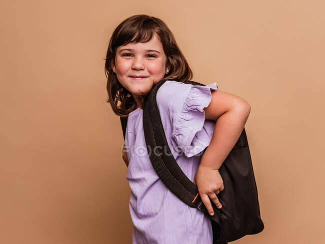 Carino scolaro in piedi su sfondo marrone in studio e guardando la fotocamera — Foto stock