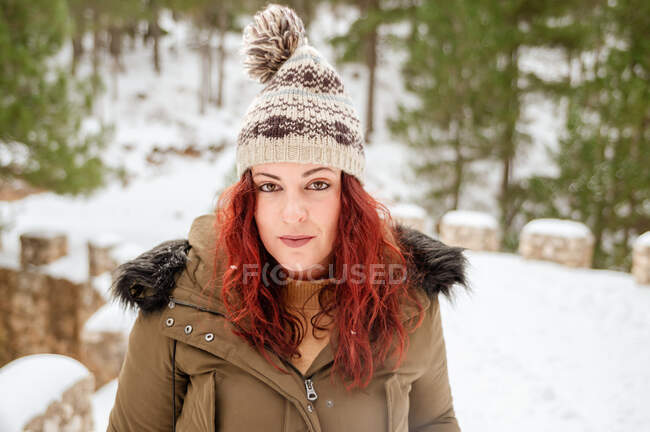 Serene female with snow on hat and hair looking at camera in winter forest — Stock Photo