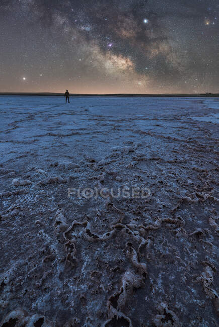 Silhouette eines Forschers, der in einer trockenen Salzlagune vor dem Hintergrund des Sternenhimmels mit glühender Milchstraße in der Nacht steht — Stockfoto