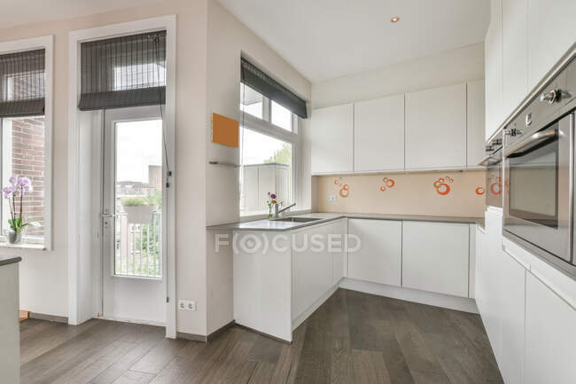 Diseño interior de cocina minimalista de planta abierta con electrodomésticos incorporados y armarios blancos en apartamento de estilo loft moderno con estructura geométrica inusual - foto de stock