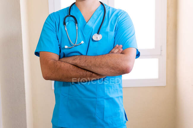 Médico masculino anónimo en uniforme azul y con estetoscopio de pie en la clínica - foto de stock