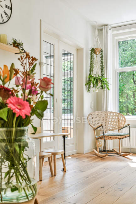 В стильной комнате с экологически чистым интерьером, деревянным полом и зелеными растениями при дневном освещении в доме, рядом с окном стоит кресло. — стоковое фото