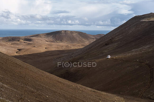 Malerischer Blick auf in den Bergen geparkte Fahrzeuge gegen den Fagradalsfjall und das Meer mit Horizont unter wolkenverhangenem Himmel in Island — Stockfoto