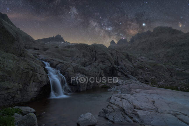 Magnificent scenery of foamy splashing waterfall streaming among rough rocky terrain under night starry sky with bright glowing Milky Way — Stock Photo