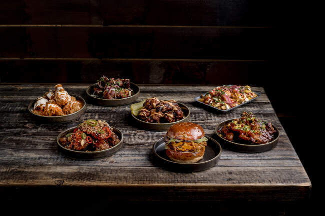 Von oben appetitliche Chicken Wings in BBQ-Sauce in der Nähe von Burger und Käse Pommes auf Holztisch im Restaurant platziert — Stockfoto
