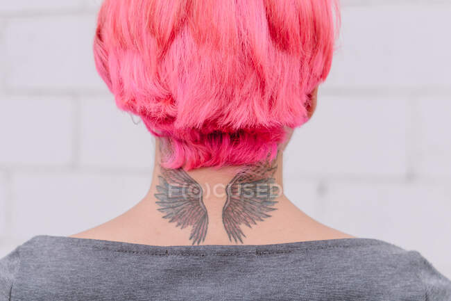 Voltar vista colheita fêmea irreconhecível com cabelo tingido e tatuagem de asas no pescoço em pé perto da parede branca — Fotografia de Stock