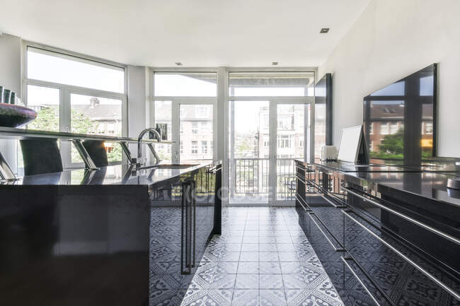 Moderno design interno della spaziosa cucina a pianta aperta con mobili neri e piastrelle ornamentali al piano e con ampie finestre panoramiche con vista sugli edifici urbani — Foto stock