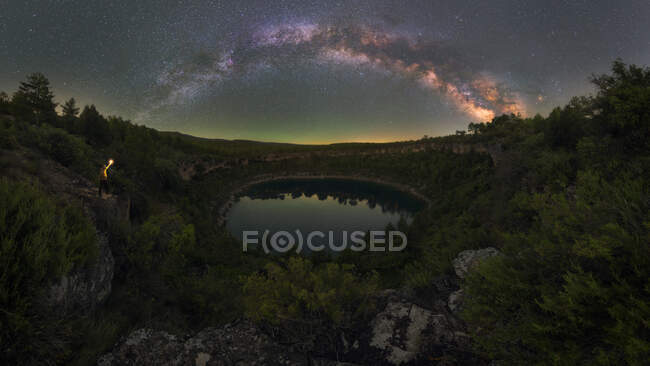 Anonymous traveler with torch contemplating lagoon among mountains under starry sky at night in Spain — Stock Photo