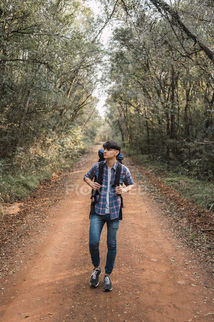 Male explorer with backpack walking on sandy path in forest during trekking and looking away — Stock Photo
