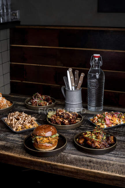 Mesa de madera servida con hamburguesas apetitosas y alas de pollo en restaurante de comida callejera - foto de stock