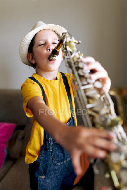 Kind mit Saxofon im Wohnzimmer steht gegen Fenster im Zimmer — Stockfoto