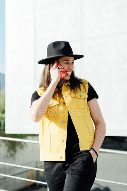 Content female in stylish clothes standing in city street and talking on cellphone while looking away — Stock Photo