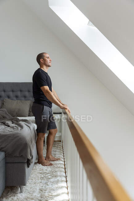 Mann steht nach dem Aufwachen morgens zu Hause in Bettnähe und betrachtet Blicke aus Fenstern — Stockfoto