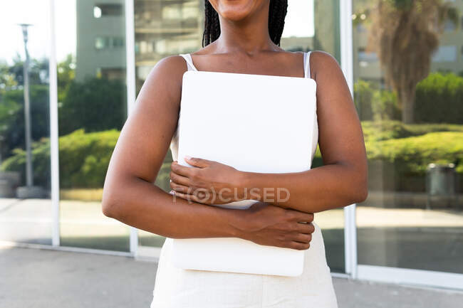 Anonymous African American female freelancer with braids and white netbook standing in street in Barcelona and looking at camera — Stock Photo